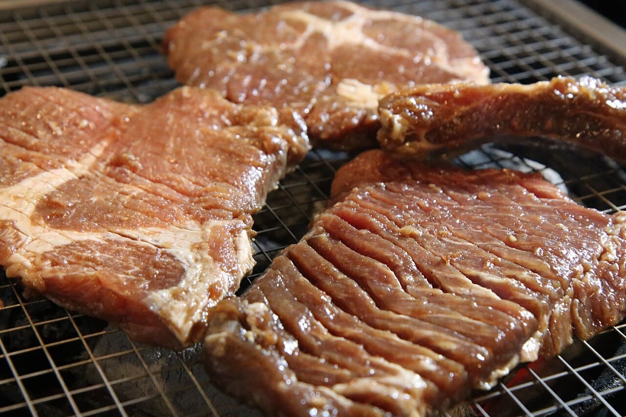 Các lát 갈비 sườn bò ướp gia vị trên giá nướng, bóng loáng với nước ướp
