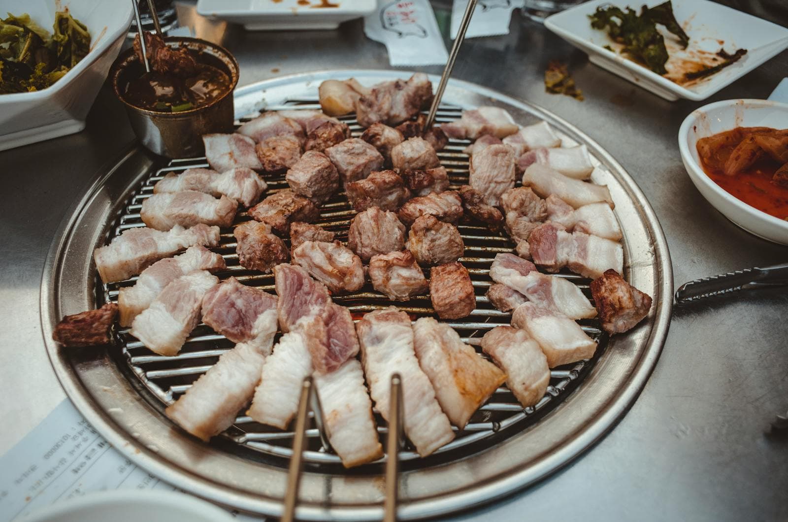 Các miếng 삼겹살 đã cắt nhỏ vừa ăn đang nướng trên vỉ nướng Hàn Quốc tròn