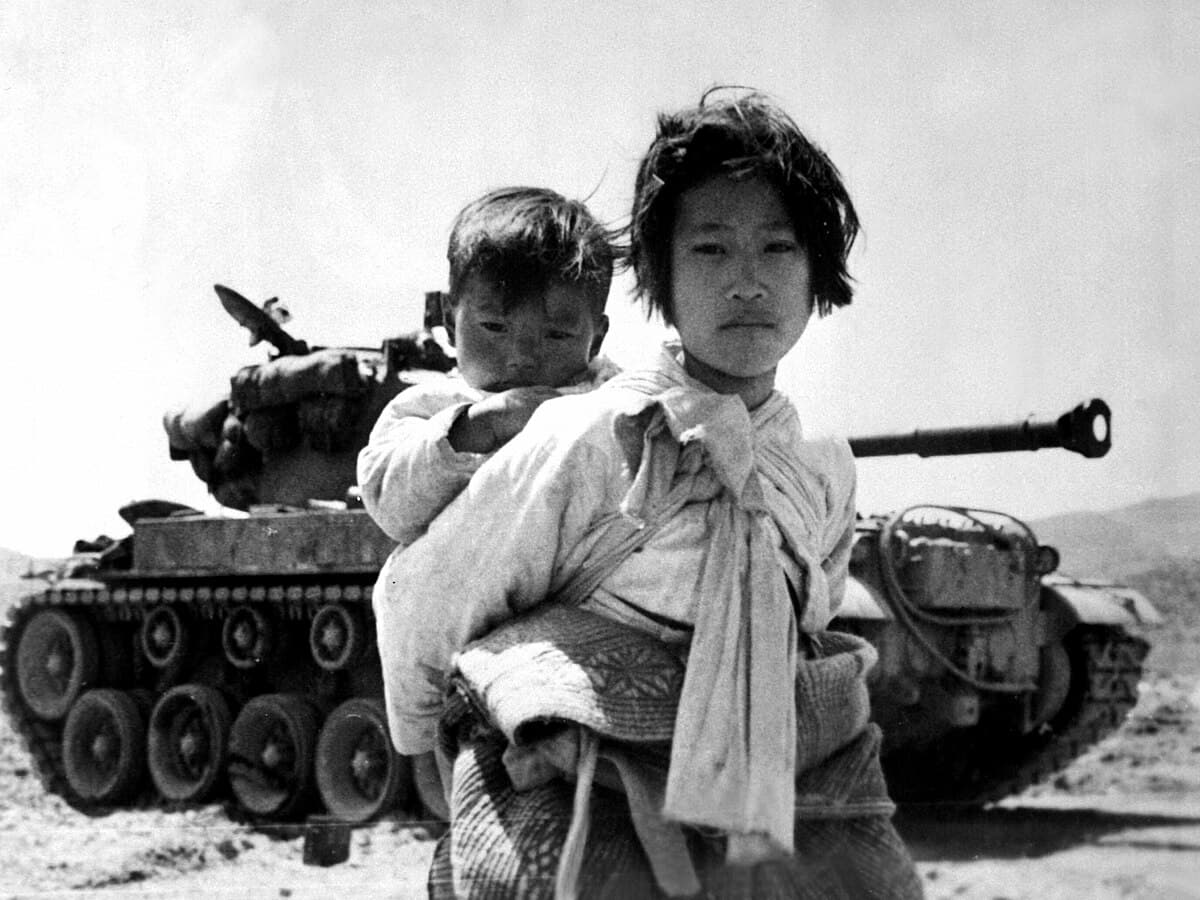 1951年6月,一名韩国女孩背着弟弟,走过幸州附近一辆抛锚的M46巴顿坦克